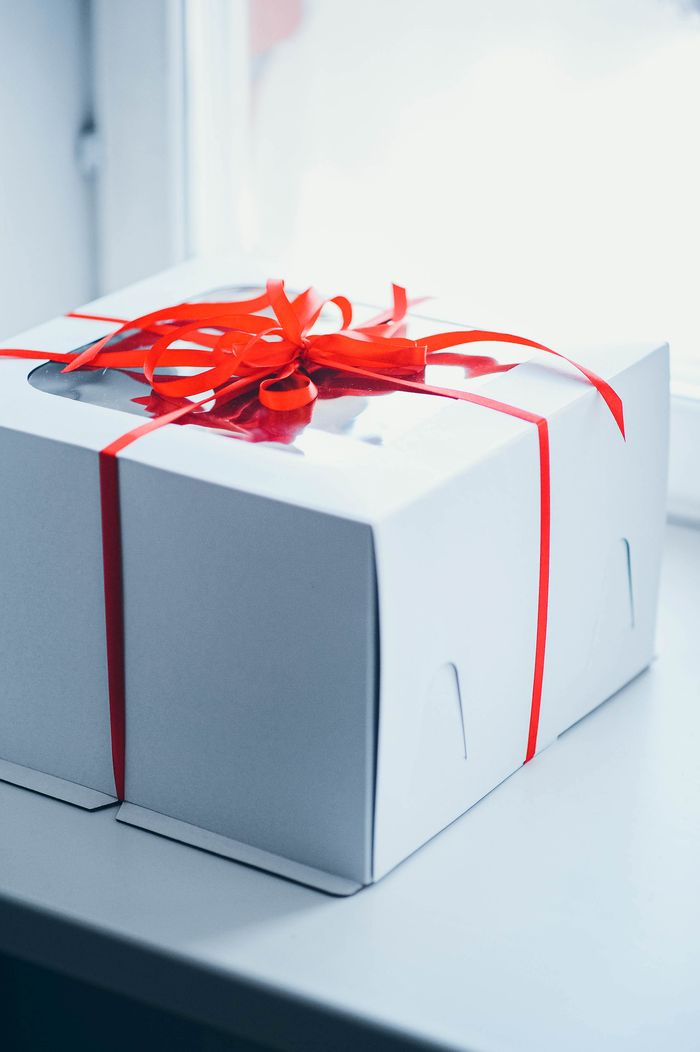 Stylish white gift box tied with a red ribbon resting on a bright windowsill, perfect for special occasions.