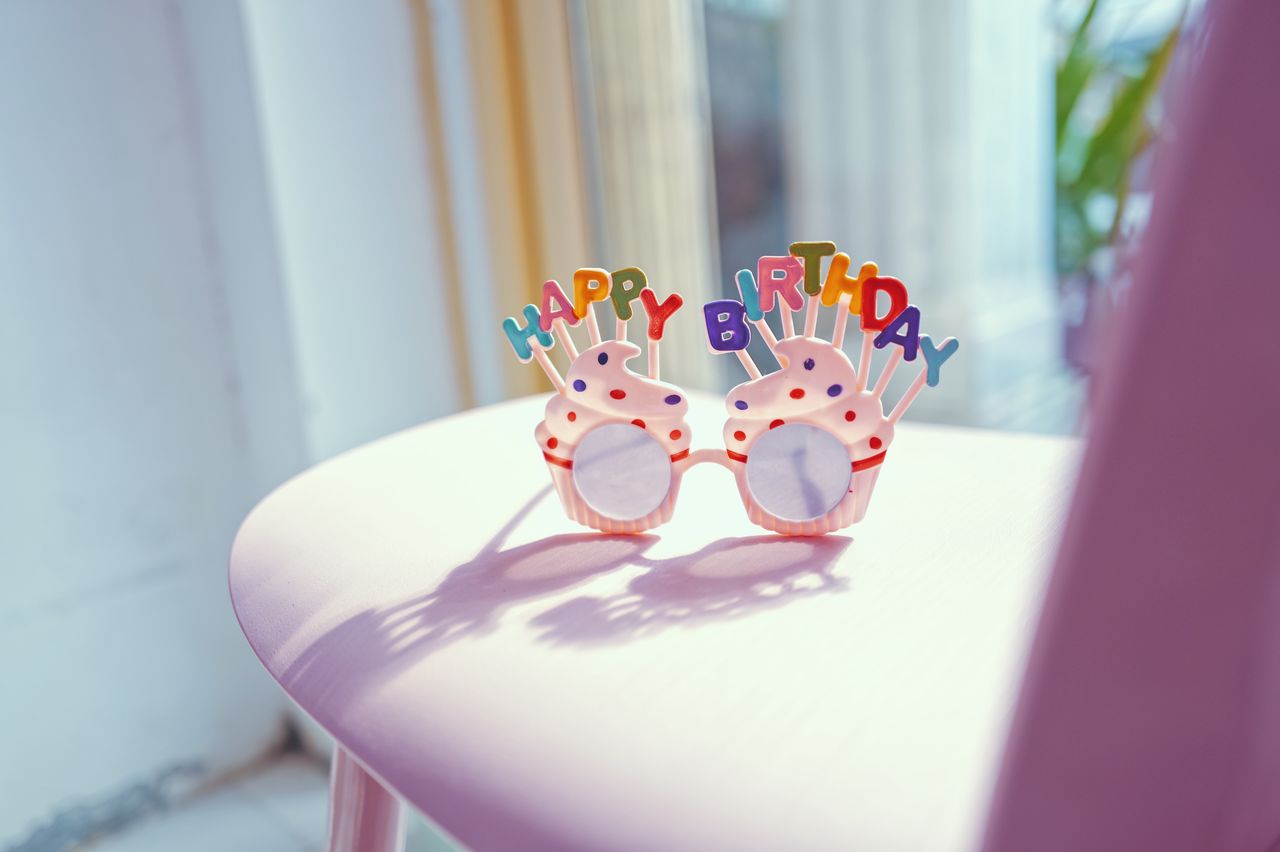ours-journey Colorful birthday glasses with 'Happy Birthday' sign on a pink chair in bright sunlight.