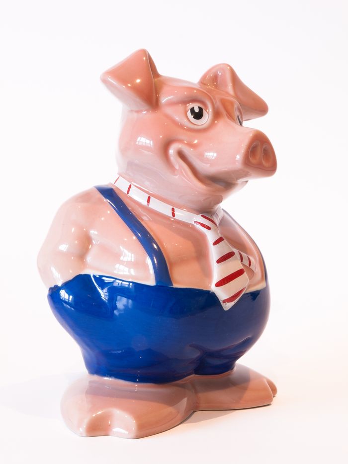 Colorful ceramic pig figurine in overalls and tie on a white background.