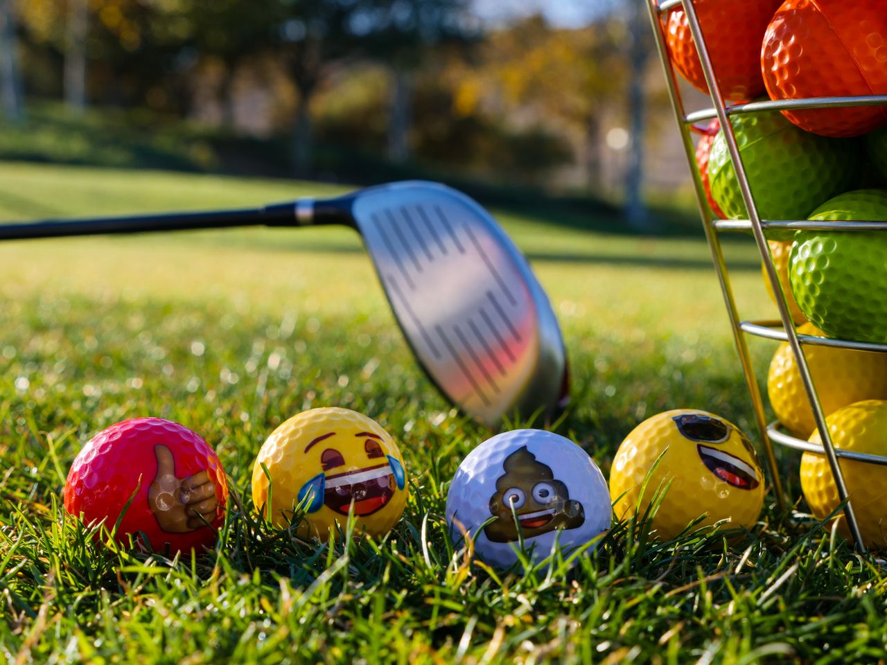 Bright golf balls with emojis on grass beside a club and bucket, embracing fun on the course.